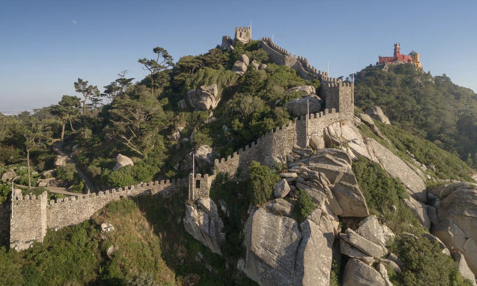 Parques de Sintra, showing Moorish Castle medieval ramparts with Pena Palace on the Sintra hills, both UNESCO World Heritage monuments under one governance body.