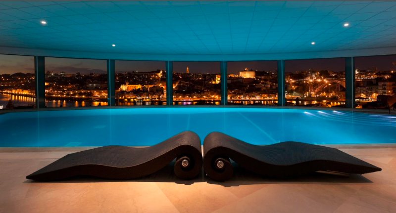 The Yeatman indoor infinity pool at night with Porto city lights through arched glass, part of the 2,000 m² Wine Spa with 10 treatment rooms used by BTQ Events as a wellness anchor inside multi-day corporate programmes